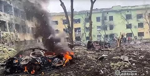 SASARAN BOM: Sebuah kereta terbakar di luar bangunan hospital kanak-kanak yang dibedil oleh tentera Russia di bandar Mariupol di tenggara Ukraine. - Foto-Foto AFP CARI PERLINDUNGAN: Sekumpulan warga Ukraine tiba di sempadan negara itu dengan Poland d
