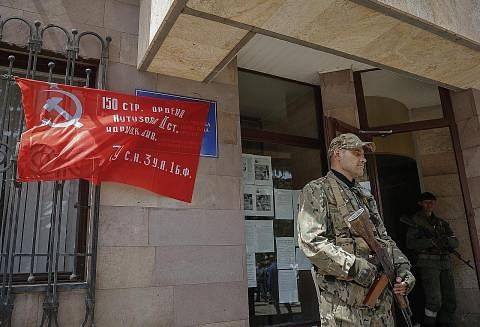 OFENSIF RUSSIA: Seorang anggota militia Republik Rakyat Donetsk mengawal pintu masuk bangunan pentadbiran bandar Svitlodarsk, di wilayah Donetsk (gambar kiri), Khamis lalu. Tentera Russia menawan Svetlodarsk, yang terletak 80 km ke barat laut Severod