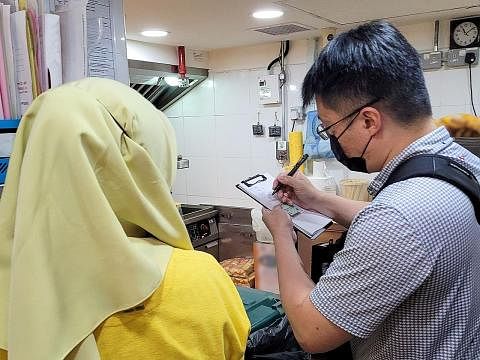 AMBIL TINDAKAN: Pegawai penguatkuasaan Agensi Makanan Singapura (kanan) mencatatkan butiran terhadap pengendali makanan. - Foto SFA