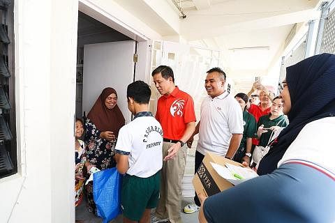 AGIH HABUAN: Encik Chan Chun Sing (berbaju merah) dan Encik Shahrael Taha menyertai seorang pelajar Sekolah Rendah Casuarina memberi beg habuan kepada seorang benefisiari Pasir Ris Care Store, Cik Sarah Ismail, pada Sabtu. - Foto ZAOBAO