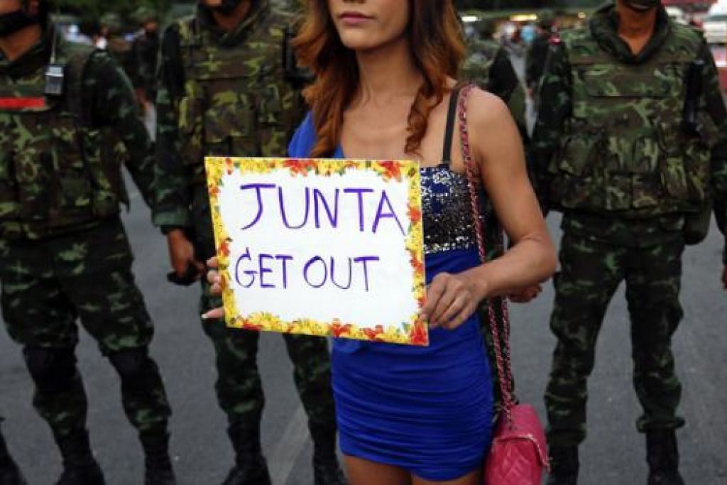 BANTAH: Seorang penunjuk perasaan berdiri di depan askar di Monumen Kemenangan di Bangkok kelmarin sambil memegang mesej menggesa pihak junta berundur daripada pemerintahan. - Foto REUTERS
