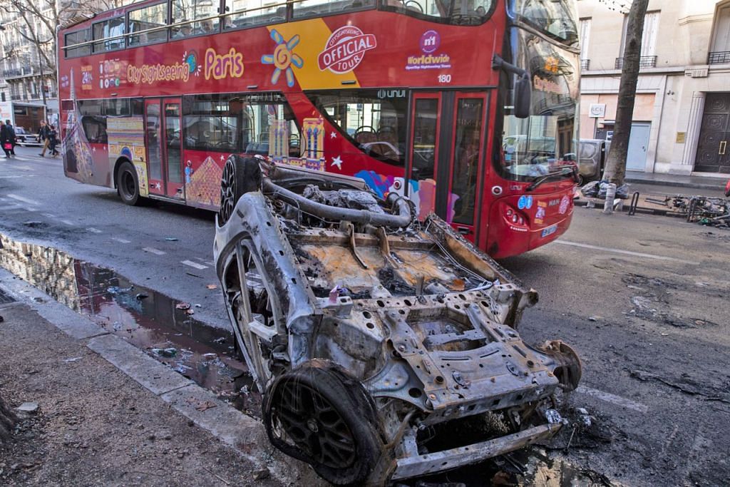 KESAN RUSUHAN: Sebuah bas pelancong melintasi bangkai kereta yang terbakar ekoran rusuhan di Paris hujung minggu lalu. - Foto EPA-EFE