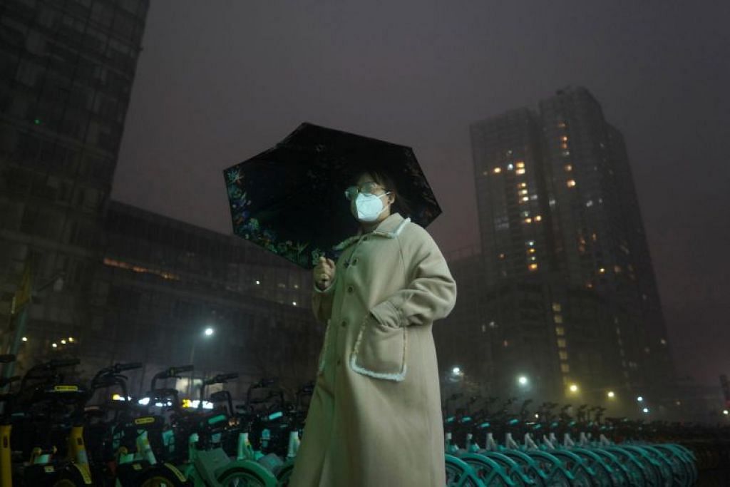 Seorang wanita yang berpelitup, berjalan di tengah-tengah dsitrik pusat perniagaan di Beijing pada 29 Februari dalam cuaca hujan. 
