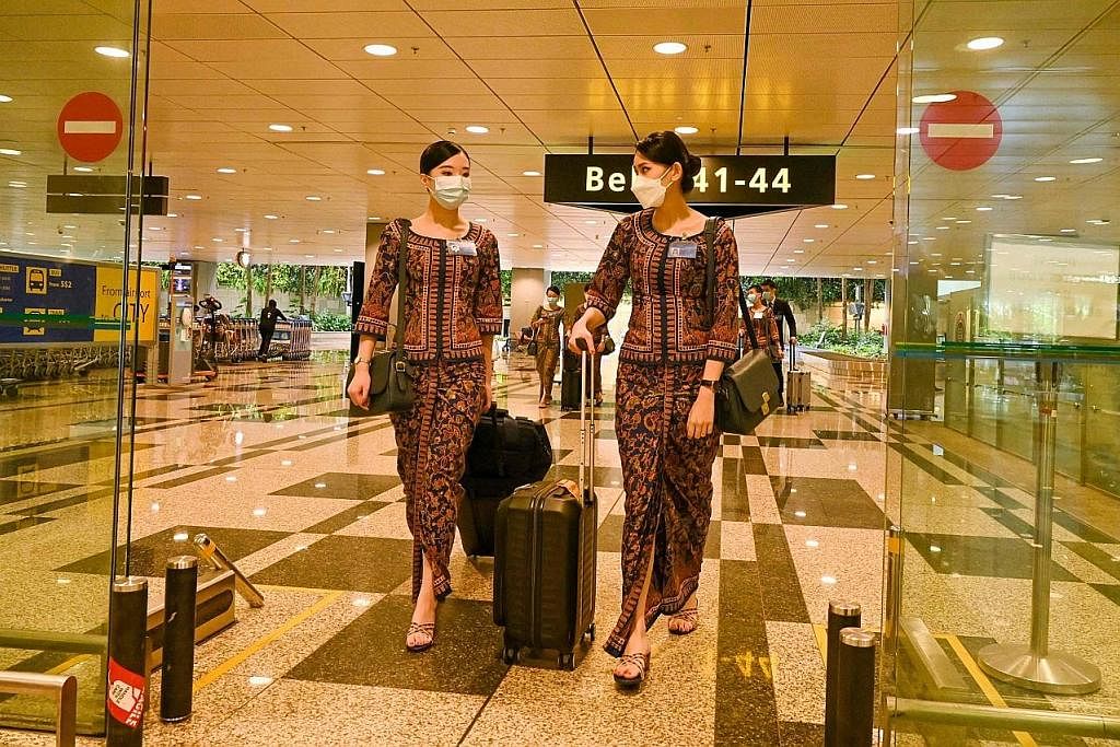 PERIKSA TIKET: Seorang kakitangan di Lapangan Terbang Antarabangsa Changi memeriksa tiket digital penumpang sebelum membenarkan mereka membuat daftar masuk sendiri di dewan berlepas. - Foto-foto AFP SELESAI BERTUGAS: Kru Singapore Airlines tiba di La