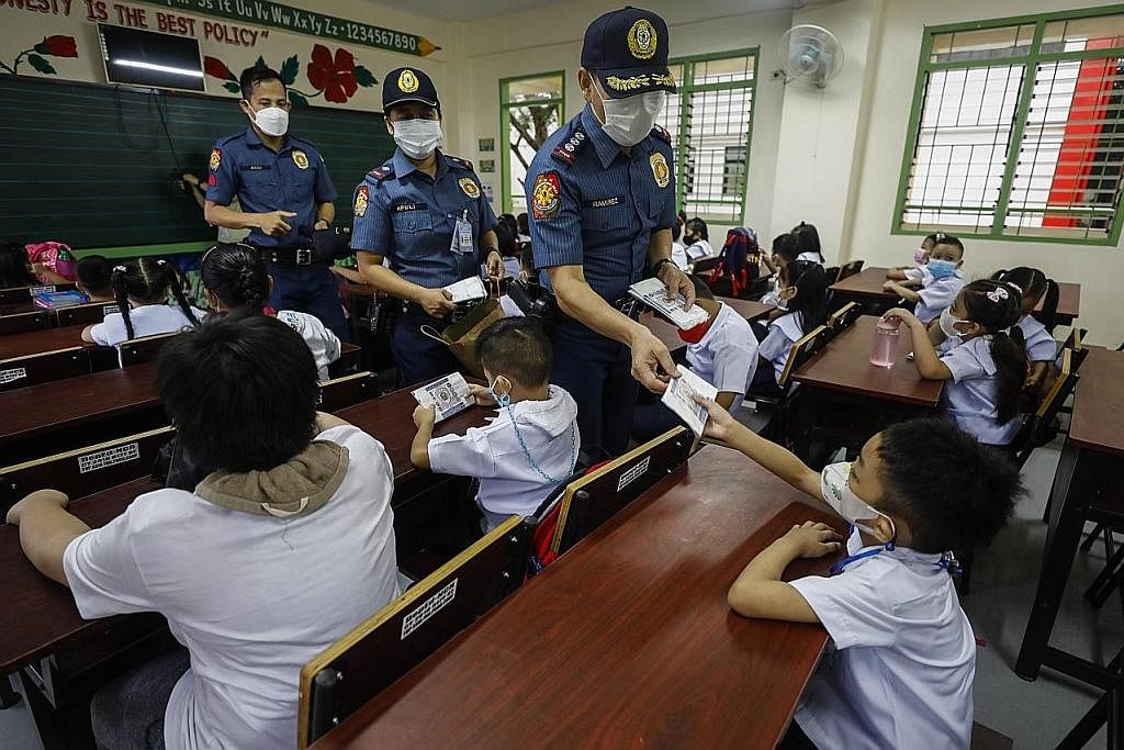 EDAR PELITUP: Pegawai polis mengedarkan pelitup muka percuma kepada murid-murid yang kembali belajar secara fizikal sejak Isnin lalu.