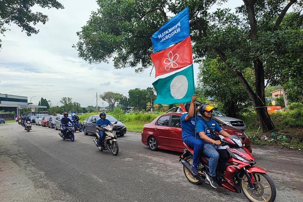 KIAN HANGAT: Seorang pembonceng motosikal mengibarkan bendera Perikatan Nasional (biru) dan dua parti yang membentuknya, Parti Pribumi Bersatu Malaysia (merah) dan Parti Islam SeMalaysia (PAS) di Ipoh, Perak, dengan bahang PRU15 kian terasa di serata