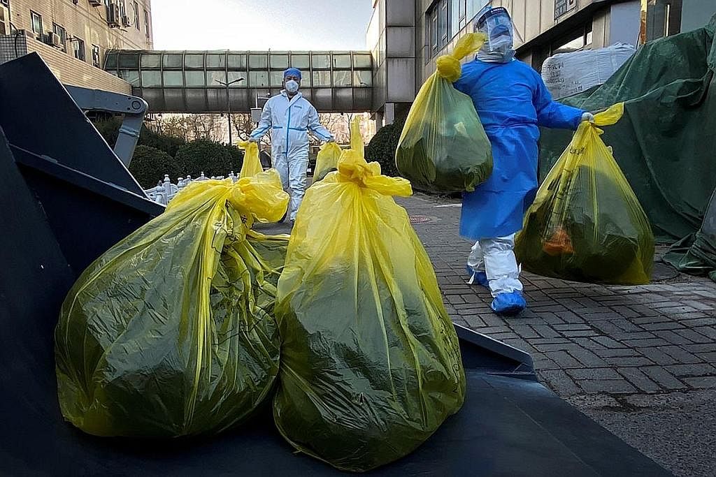 LONGGAR SEKATAN: Pekerja yang memakai pakaian perlindungan mengalihkan beg sisa perubatan di luar bangunan tempat penduduk mengasingkan diri di rumah ketika wabak penyakit koronavirus (Covid-19) menular di Beijing. - Foto REUTERS