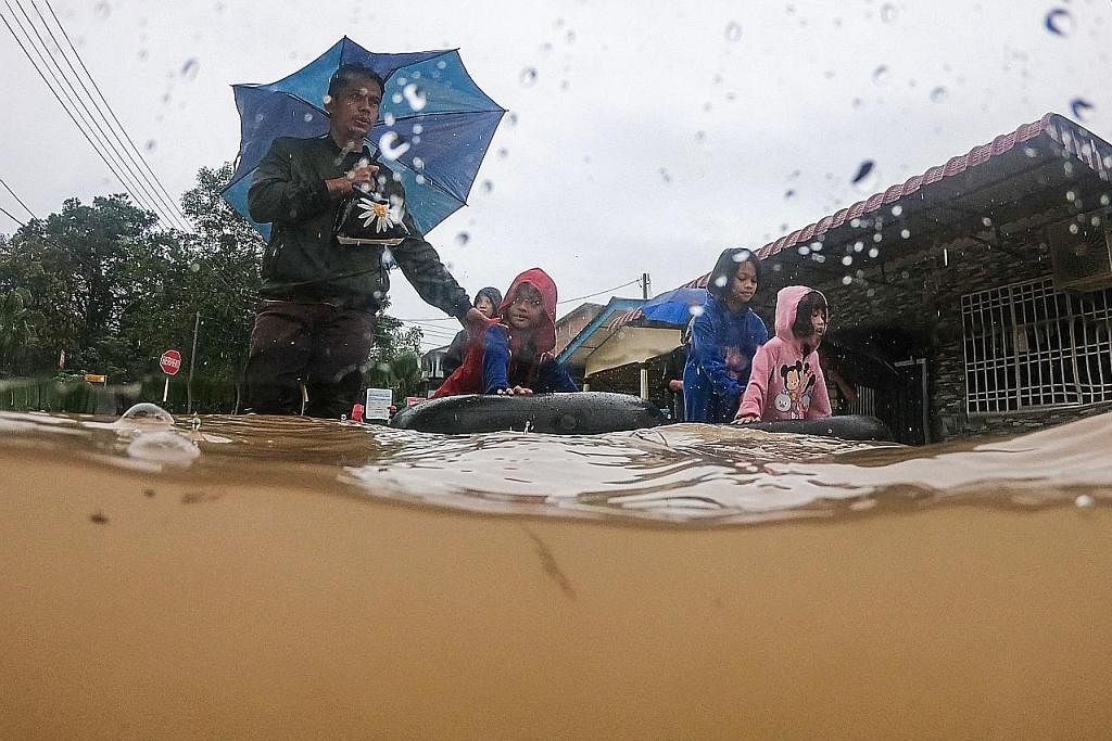 SELAMATKAN DIRI: Sebuah keluarga mengharungi air banjir selepas keluar dari rumah mereka di Yong Peng, Johor, pada Sabtu. Lebih 37,000 penduduk, di sembilan daerah di Johor terjejas akibat banjir, setakat 8 pagi Sabtu. - Foto AFP